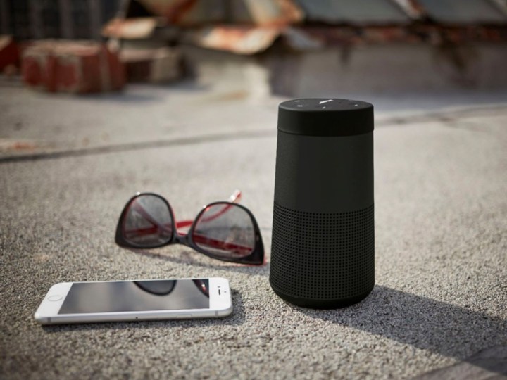 Bose SoundLink Revolve II on the sidewalk with glasses and smartphone.