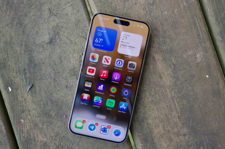 An iPhone 15 Pro Max, lying on a wood floor with its display on.