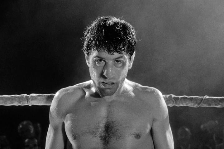 Robert De Niro stands near the ropes of a boxing ring in Raging Bull.