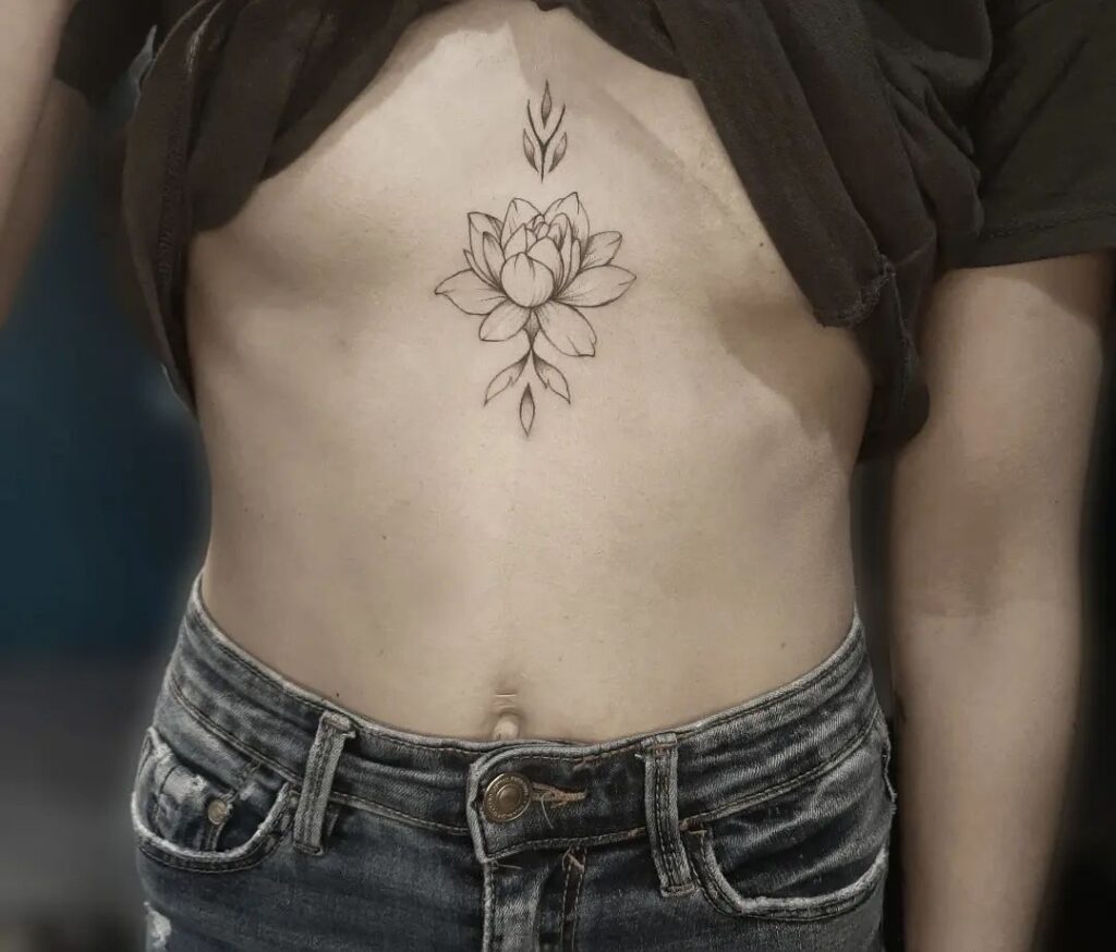 Minimalist under-breast tattoo featuring a lotus flower with subtle leaf accents, symbolizing purity and growth