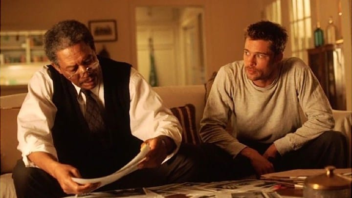 In a scene from Seven, Morgan Freeman and Brad Pitt sit on the couch together and look at the papers.