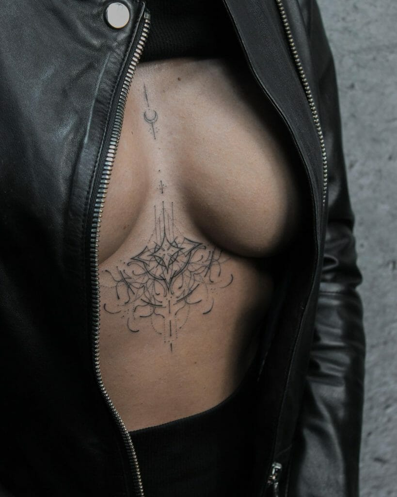 Minimalist under-breast tattoo with fine line and dot work, creating a symmetrical, lace-inspired design beneath the breast