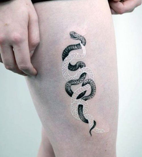 A black and white snake tattoo featuring geometric scales, wrapping around the thigh with contrasting dark and light ink