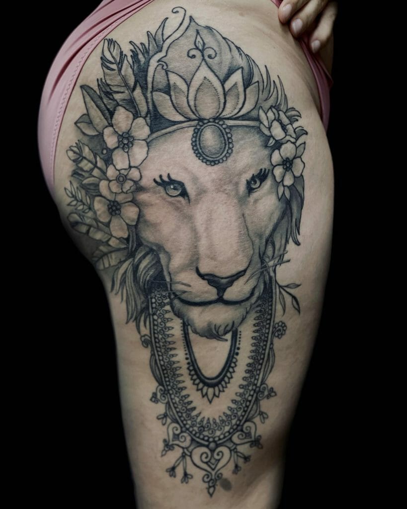 Thigh tattoo of a lion with a lotus crown, floral details, and intricate jewelry, symbolizing strength, spirituality, and grace