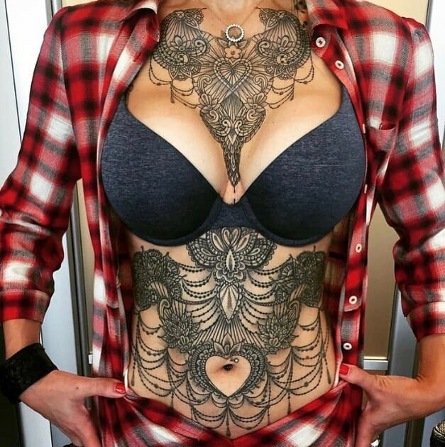 Full chest and stomach lace tattoo with intricate heart, floral motifs, and hanging chain details, creating a corset-like effect