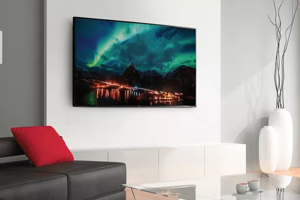 A TCL 65-inch Class 4-Series 4K TV is mounted on the living room wall with an image of the Northern Lights on the screen.