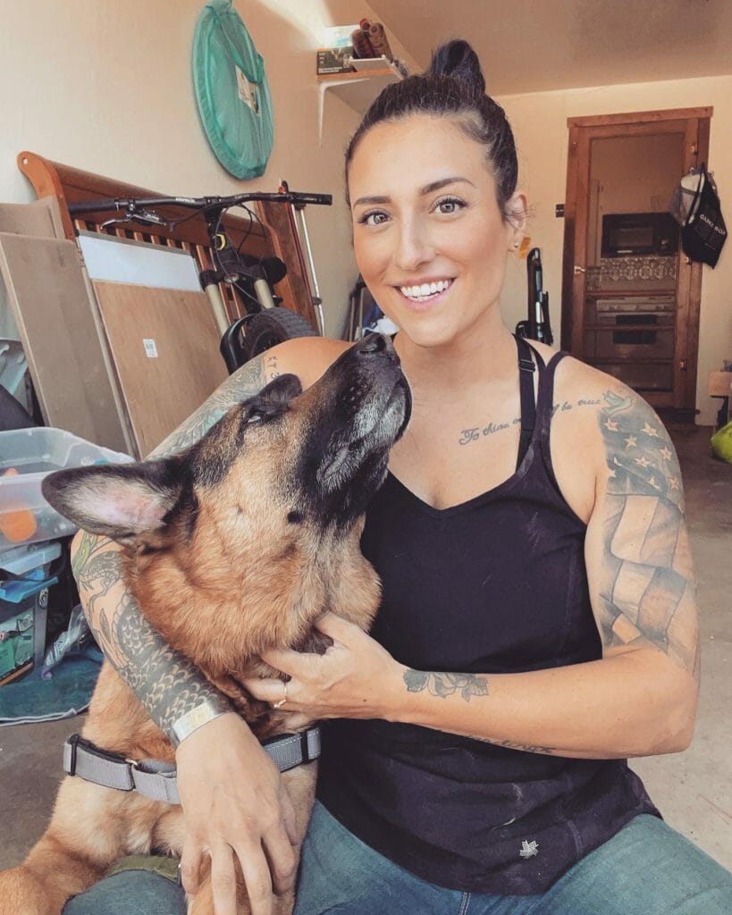 Woman with geometric military-inspired sleeve tattoo sitting with her German Shepherd, featuring intricate designs and personal symbols