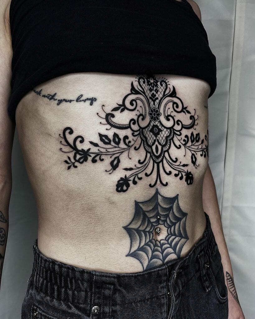 Bold under-breast tattoo with ornate lace-inspired design and black ink detailing, featuring floral patterns and decorative swirls