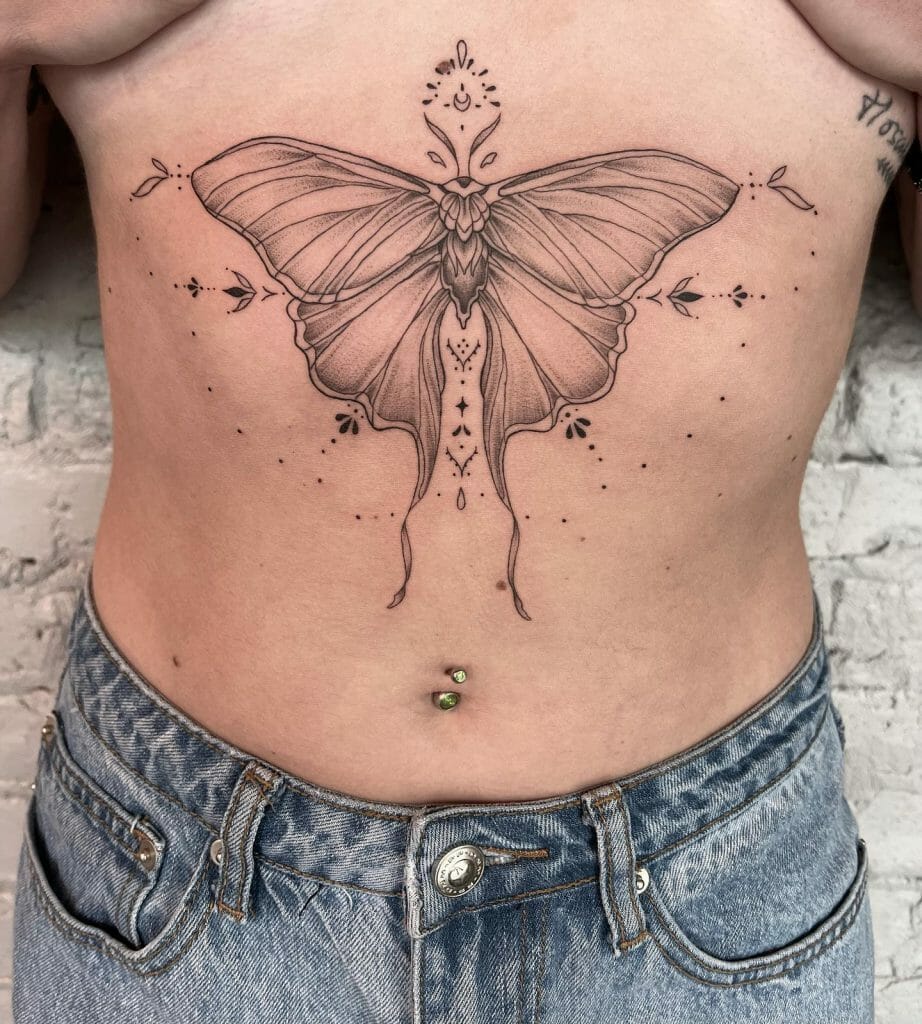 Under-breast tattoo featuring a detailed lunar moth design with delicate shading, fine lines, and decorative accents