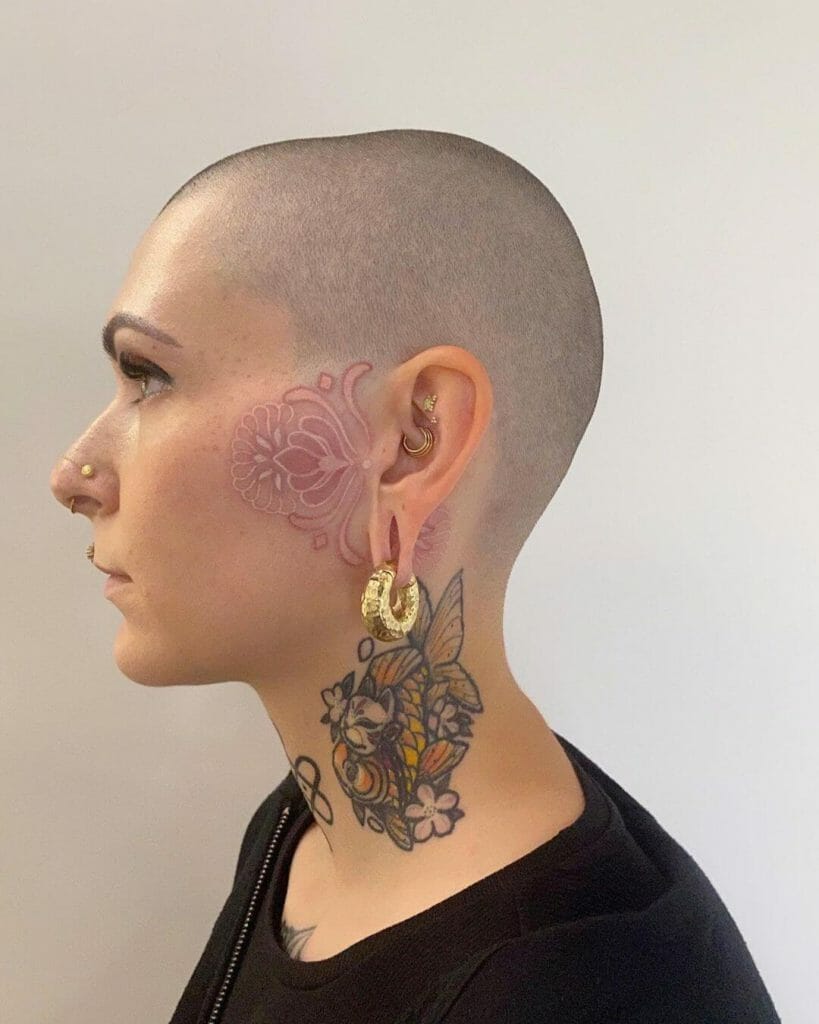 A side profile of a person showcasing a pink ornamental tattoo design on the side of the face, with a bold floral and butterfly tattoo on the neck