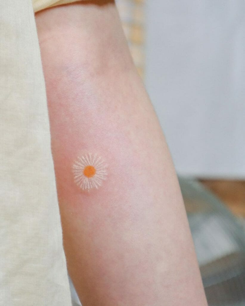 A minimalist white daisy tattoo with fine petals and an orange center, inked on the forearm, creating a soft and delicate look on light skin