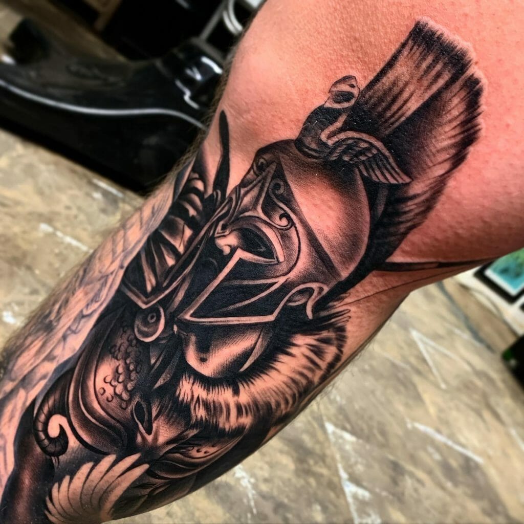 Black and grey tattoo of a Greek hoplite warrior helmet with intricate details and a feathered crest, covering the arm