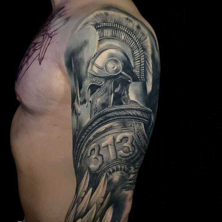 Detailed Spartan warrior helmet and shield tattoo in black and grey, featuring the number 313 on the shield, covering the upper arm and shoulder