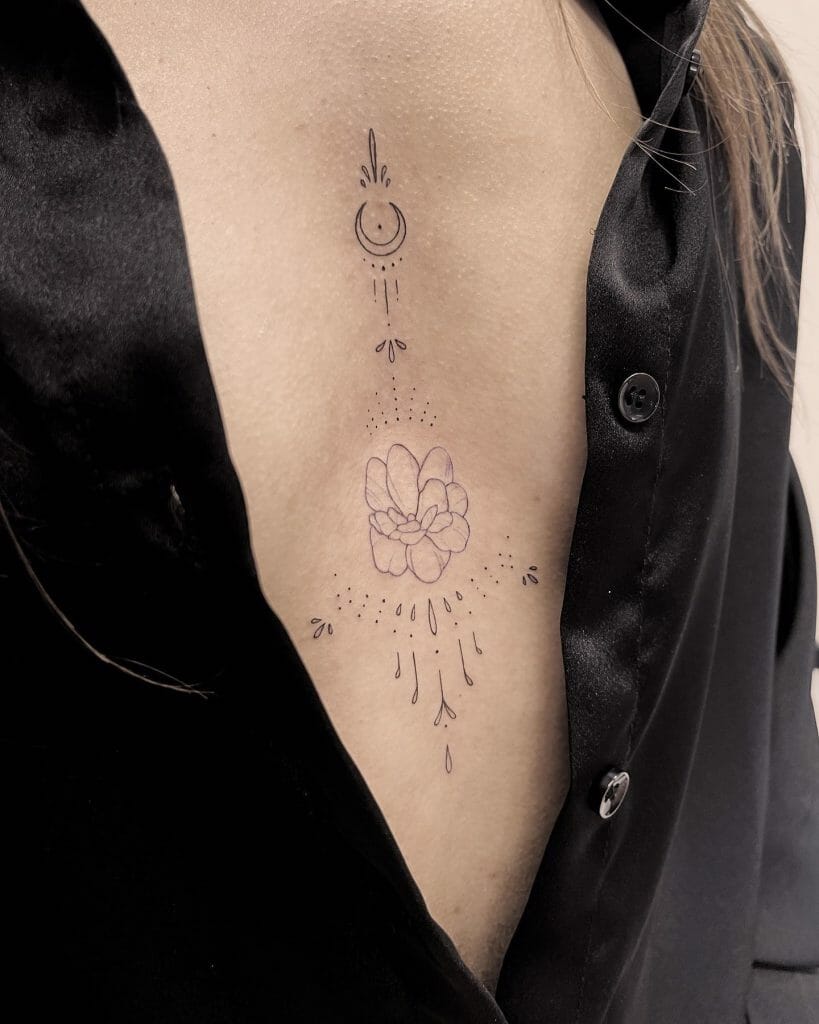 Delicate under-breast tattoo featuring a crescent moon, floral motif, and dotted accents in a minimalist design