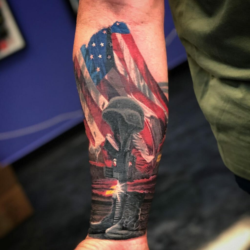 Forearm tattoo featuring a fallen soldier's battlefield cross with an American flag draped in the background, symbolizing military sacrifice