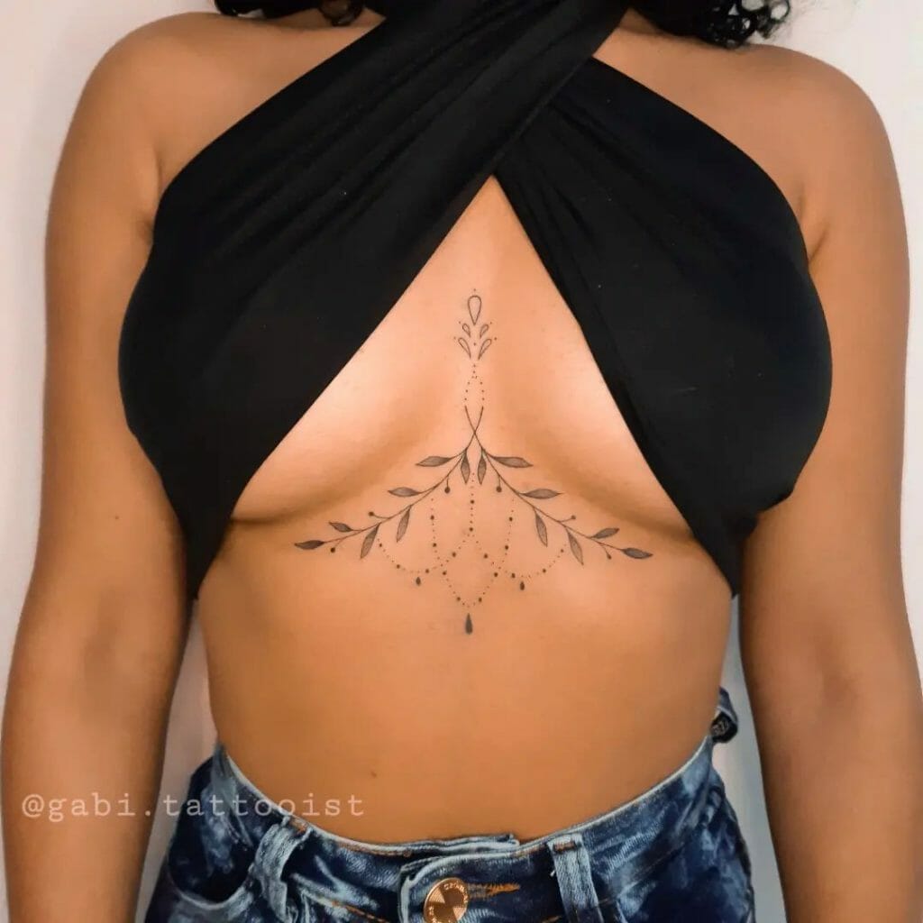 Elegant under-breast tattoo design with fine lines, delicate leaf patterns, and dotted accents, creating a soft, jewelry-like aesthetic beneath the breast