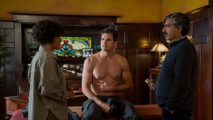 Nathan is sitting shirtless and holding his stomach while Nora and Dr. Kapoor watch in the upload.