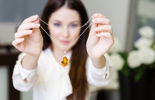 Woman holding a yellow sapphire necklace up to the camera