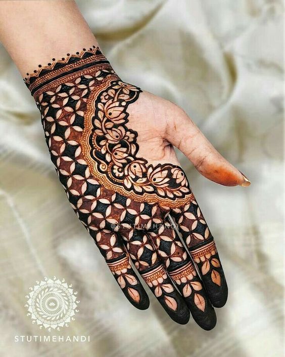 Geometric Mehndi design with intricate floral lace pattern on the back of the hand, featuring bold shading and symmetrical shapes