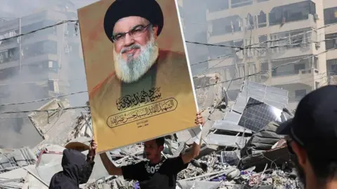 EPA A Hezbollah supporter holds a placard with Hezbollah leader Hassan Nasrallah next to the rubble of a completely destroyed building in Dahieh, a southern suburb controlled by Hezbollah, Beirut, Lebanon, 2 October 2024