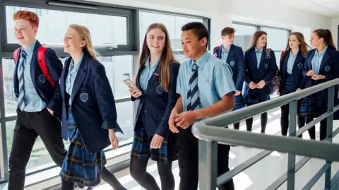 Getty Images A group of High school students walking to their next class. There is a mix of eight boys and girls and they wear blue and tartan uniforms. 