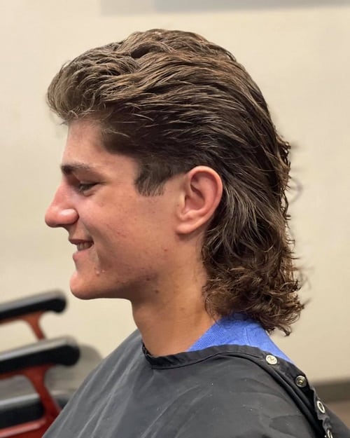 Side view of a man with a classic wet mullet haircut, featuring slicked-back hair and a voluminous long back