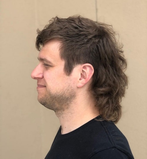 Side view of a man with a classic mullet haircut featuring natural texture and a longer, wavy back