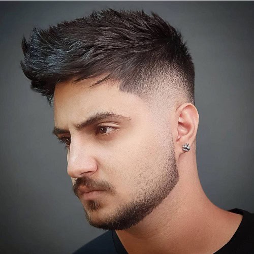 Man with a textured crew cut hairstyle and a fade, wearing a black shirt and an earring.