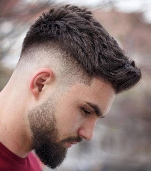 Man with a textured crew cut hairstyle featuring a high fade and a full beard, wearing a red t-shirt