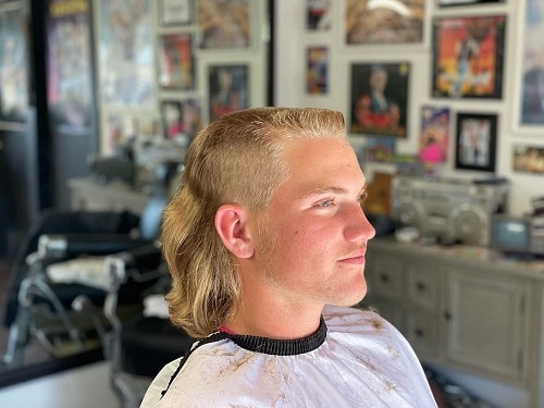 Side view of a man with a blonde traditional mullet haircut, featuring shaved sides and long back layers