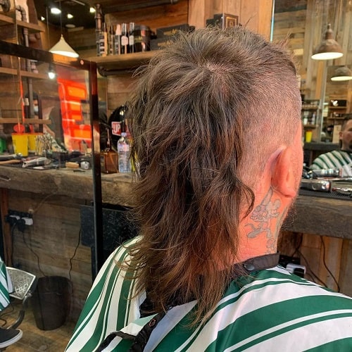 Back view of a man with a disconnected mullet featuring shaved sides and long, tousled layers at the back