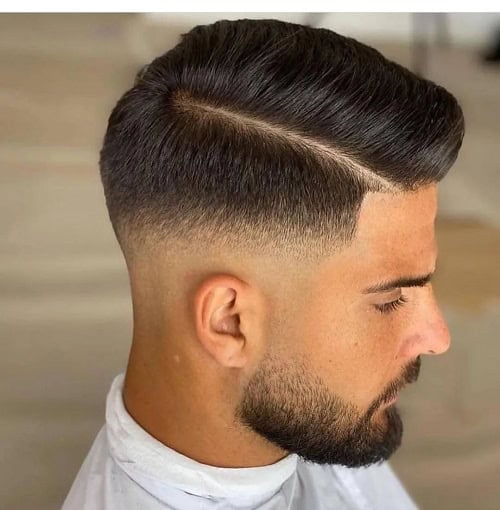 Man with a crew cut featuring a side part and a low fade, combined with a neatly trimmed beard.