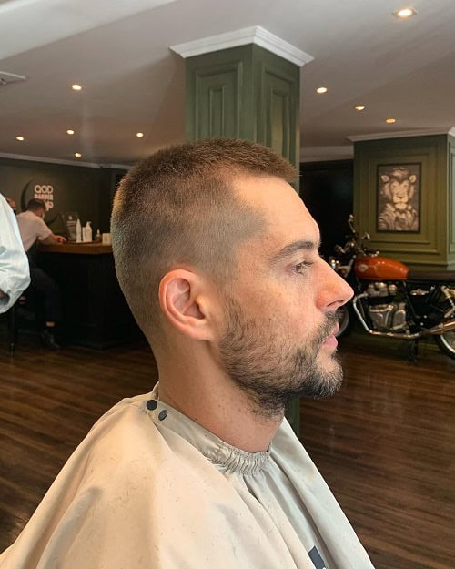 Man with a classic crew cut hairstyle, sitting in a barbershop with a clean fade and short beard.