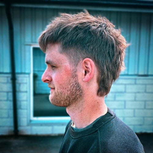 Side view of a man with a modern tapered mullet haircut, featuring short sides and a textured, longer back