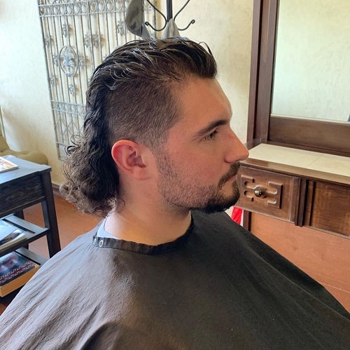 Side view of a man with a wet look mullet haircut featuring shaved sides and slicked-back long hair