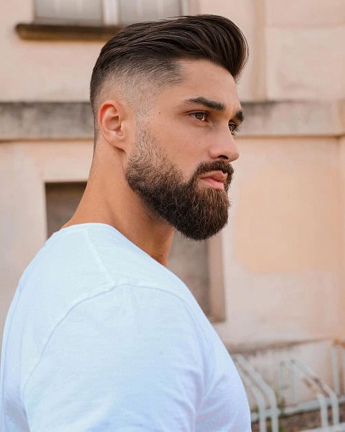 Man with a textured crew cut hairstyle featuring a high fade and full beard, wearing a white shirt