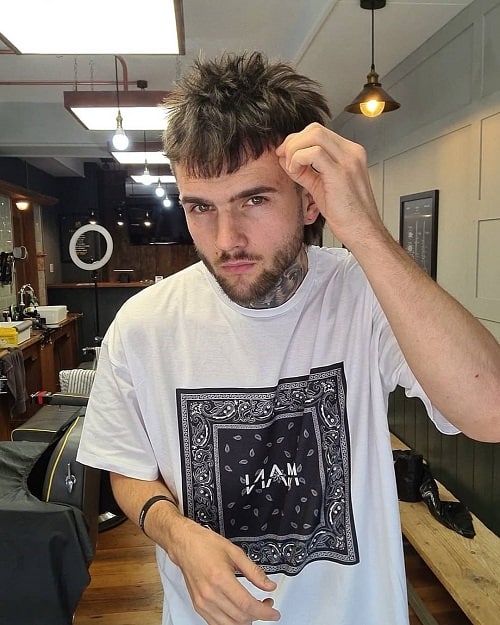 Man styling his messy mullet haircut, featuring a short fringe and textured layers for a disheveled look.