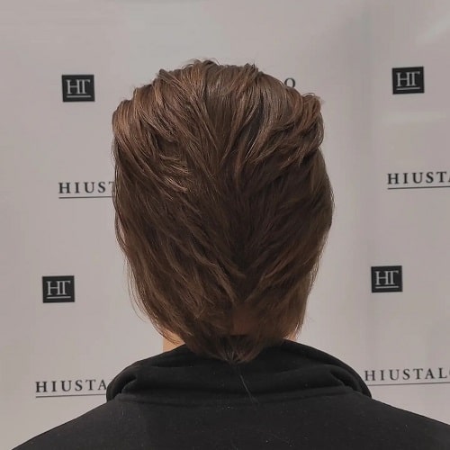 Back view of a man with a layered mullet haircut, featuring smooth layers and soft texture for a clean finish