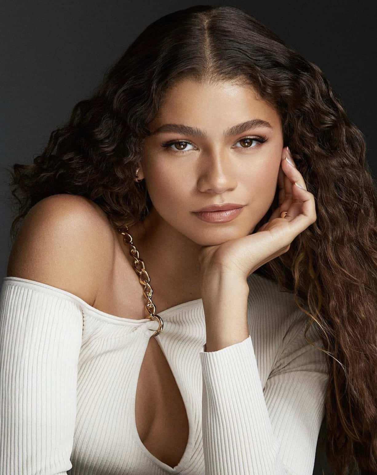 Zendaya posing in a white top with a gold chain 