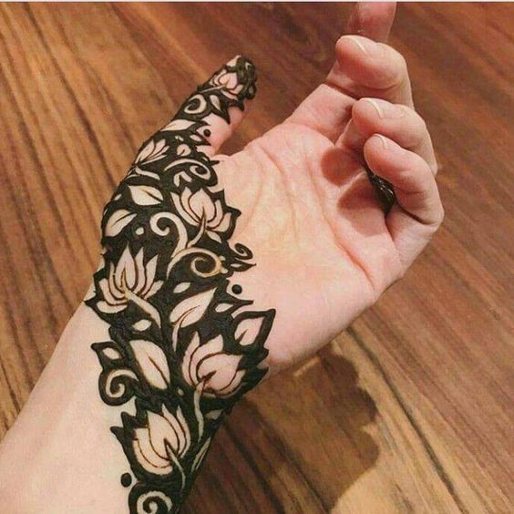 Bold floral Mehndi design with intricate flower motifs and negative space, covering the side of the hand and thumb