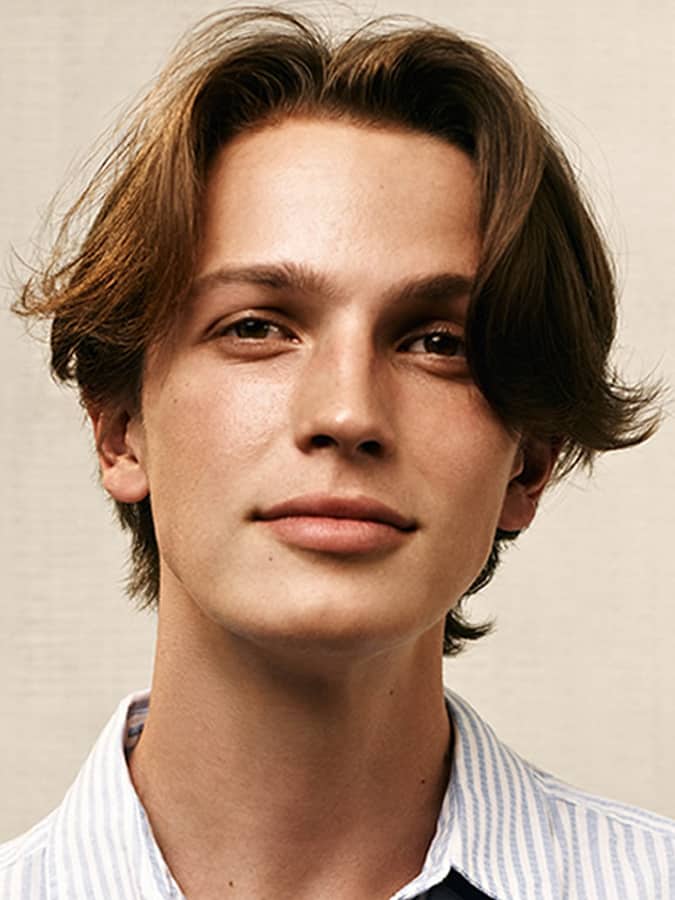 Young man with classic Eboy haircut featuring a soft middle part and layered texture, wearing a casual striped shirt