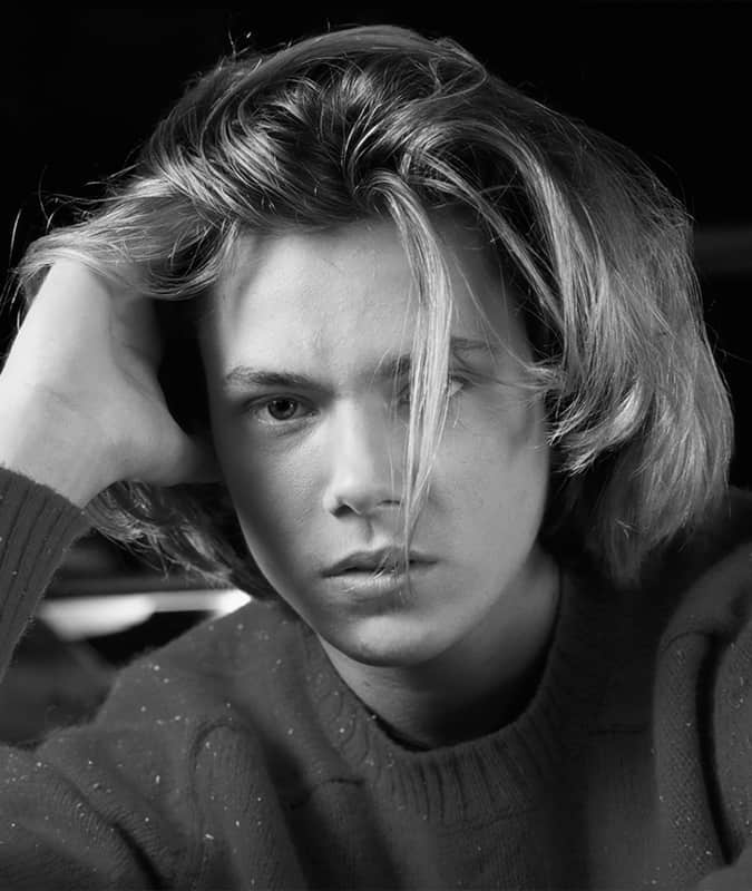 Black and white portrait of a young man with a voluminous Eboy haircut, featuring a relaxed middle part and loose layers.