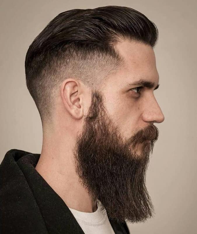 Side profile of a man with a slicked-back drop fade haircut and a long full beard.