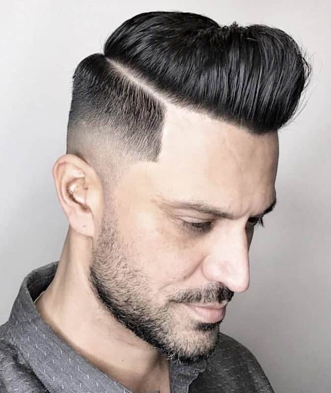 Side view of a man with a drop fade haircut, styled pompadour, and hard part.