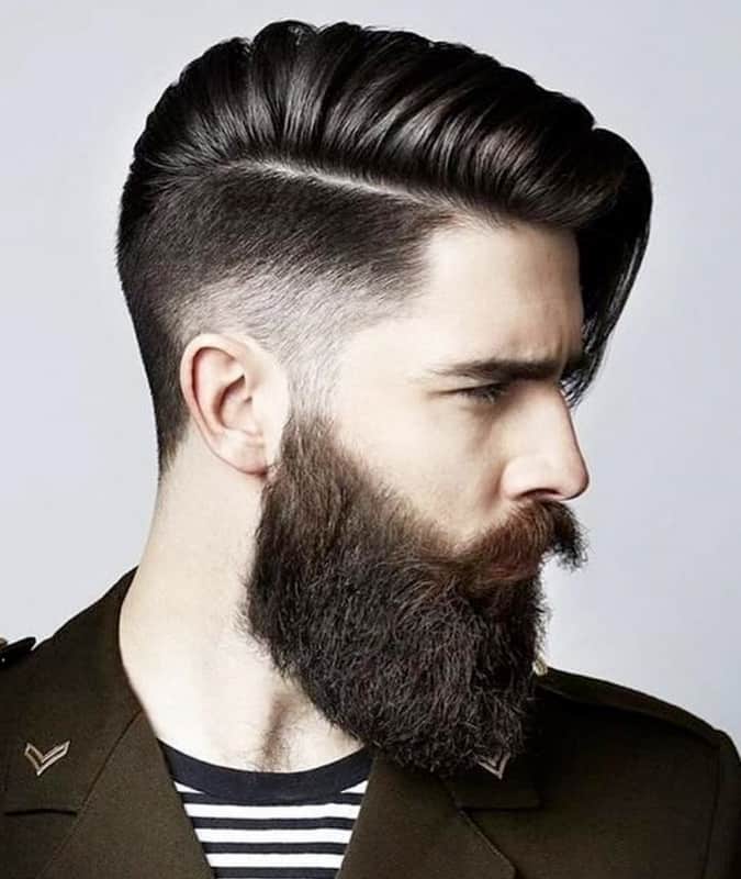 Side profile of a man with a high drop fade haircut, long comb over, and a thick, full beard.