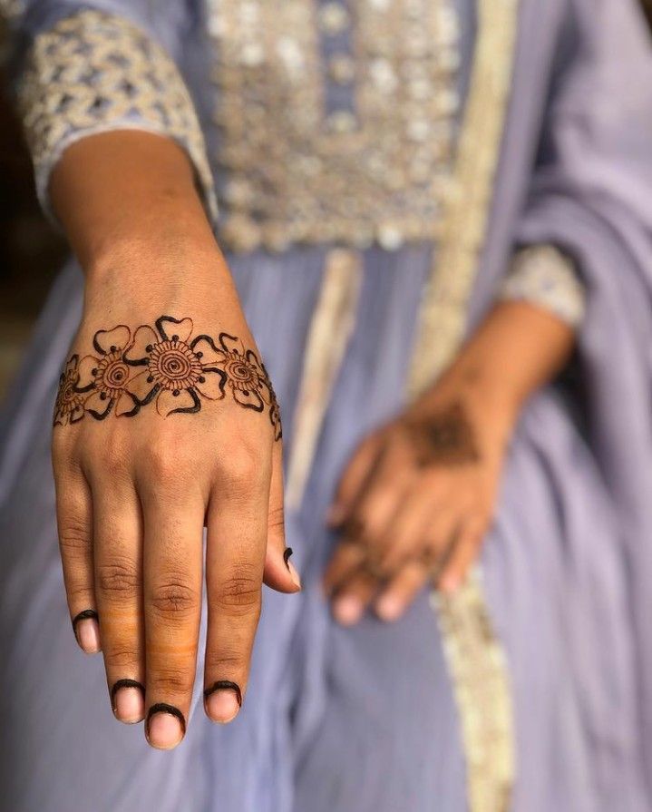 Minimalistic floral Mehndi design on the back of the hand featuring delicate flowers and curved lines, perfect for casual wear