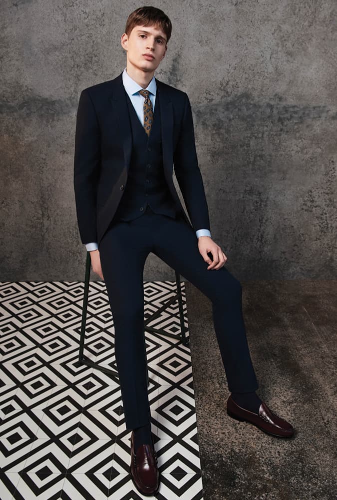 Man in a classic navy three-piece suit with a patterned tie and burgundy loafers, exuding a polished and sophisticated formal style