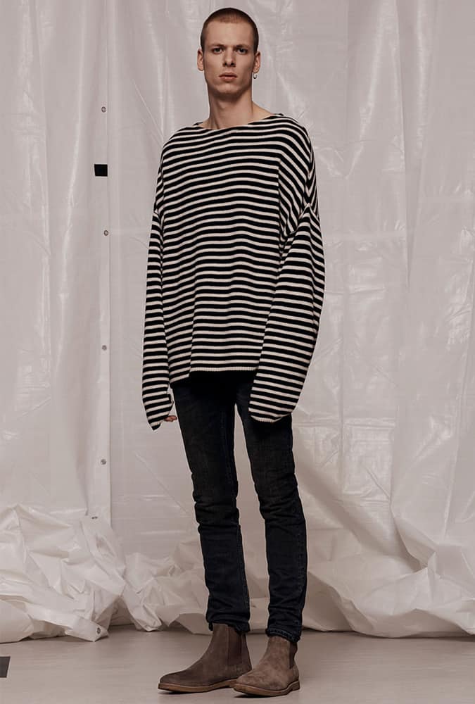 Man wearing a minimalist grunge-inspired outfit with an oversized black and white striped sweater, slim black jeans, and suede Chelsea boots