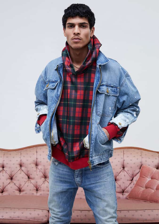 Man wearing a layered grunge-inspired outfit with a denim jacket over a red and green plaid hoodie, paired with light-wash jeans.