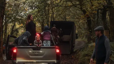 A family with small children sit in a pick up truck in the woods